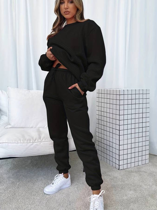 Frau in schwarzem Jogginganzug, weiße Sneaker, modernes Wohnzimmer, Freizeitmode.