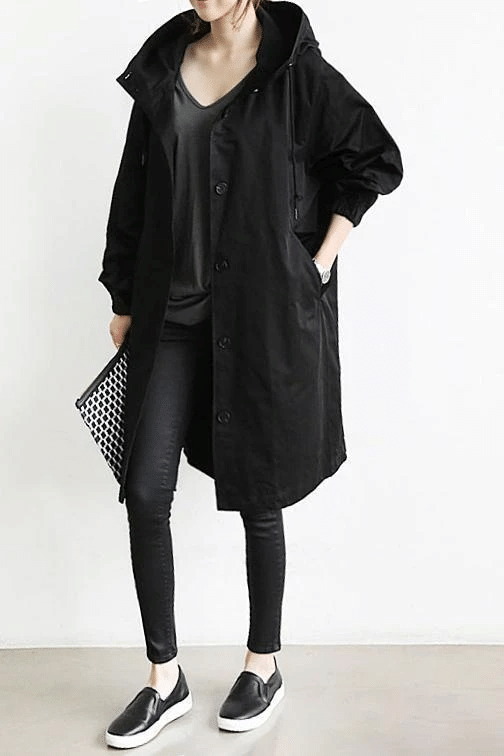 Frau in schwarzem Mantel, schwarze Leggings, Slip-On-Sneaker, modisches Outfit, lässiger Stil.