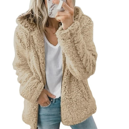 Frau in beigem Teddyfellmantel, weißem T-Shirt, blauer Jeans, Smartphone in der Hand.