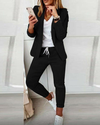 Frau in schwarzem Blazer und Jogginghose, weißes T-Shirt, Smartphone, modisch, lässig.
