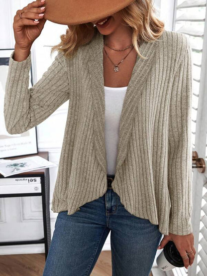 Frau in beige Strickjacke, weißem Top, blauer Jeans, braunem Hut, modisch, lässig.