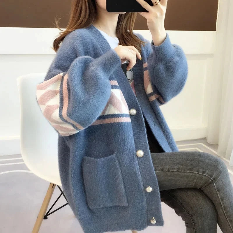 Frau trägt blauen Strickcardigan mit geometrischem Muster, Perlenknöpfen, sitzt auf weißem Stuhl.