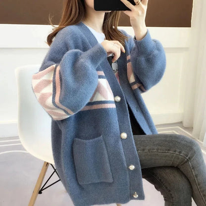Frau trägt blauen Strickcardigan mit geometrischem Muster, Perlenknöpfen, sitzt auf weißem Stuhl.