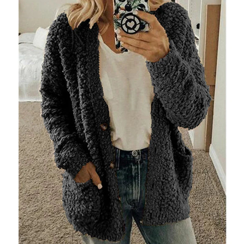Frau in grauem Strick-Cardigan, weißem T-Shirt und Jeans, hält Smartphone, gemütlicher Look.