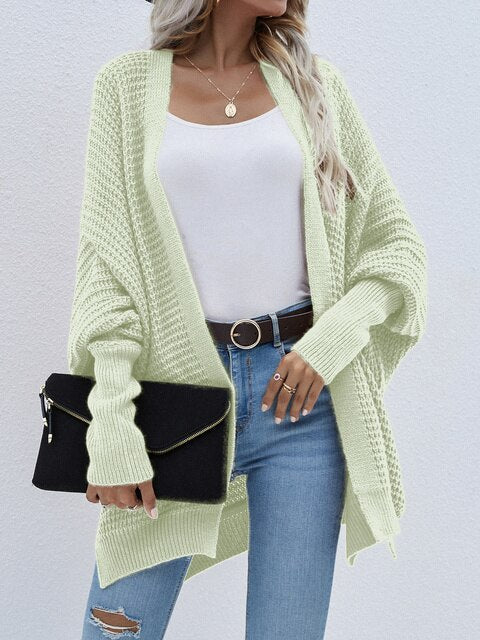 Frau in hellgrünem Strickcardigan, weißem Top, blauer Jeans, mit schwarzer Clutch.