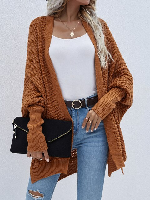 Frau trägt braunen Strick-Cardigan, weiße Bluse, blaue Jeans, schwarze Clutch, Herbstmode.