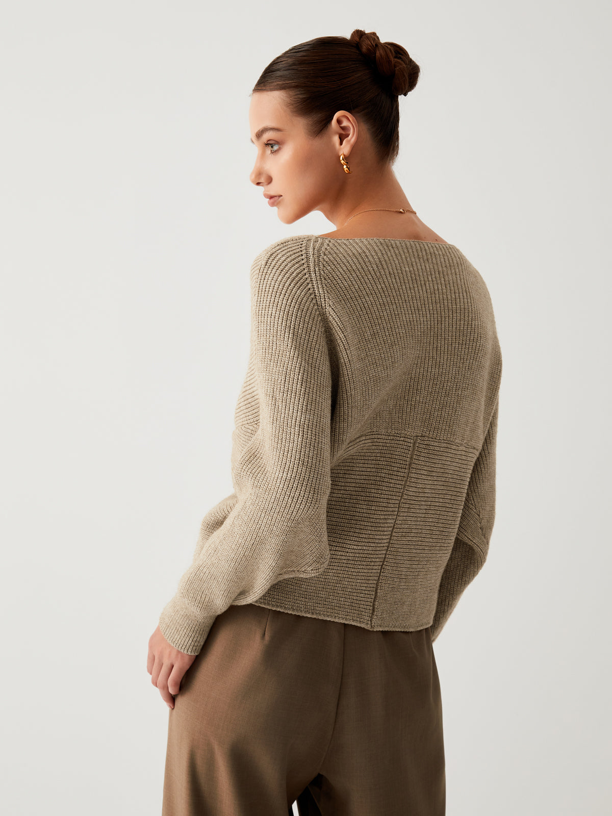 Frau in beigem Strickpullover und brauner Hose, eleganter Look, seitliches Profil.