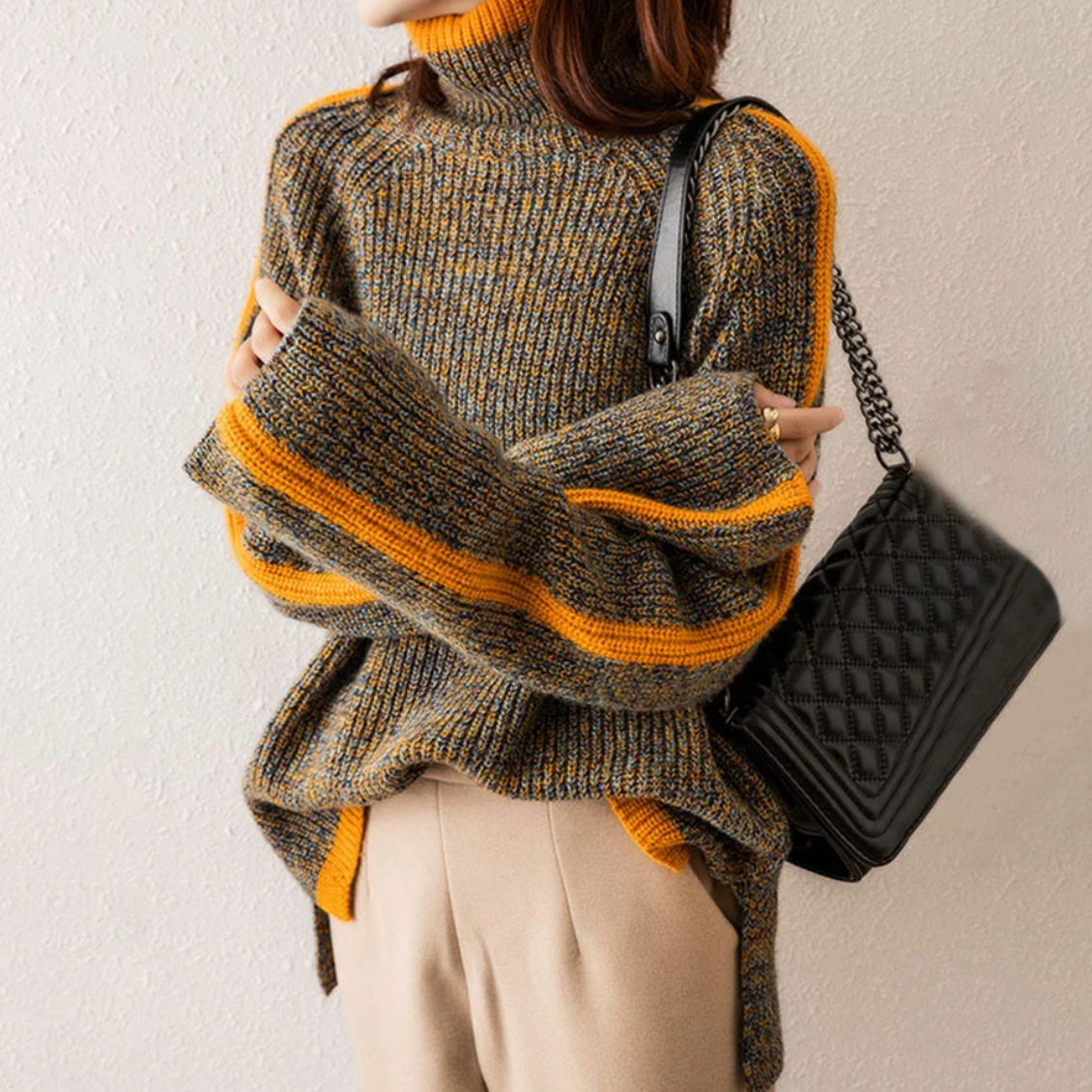Frau in gestreiftem Strickpullover mit Rollkragen, hält schwarze gesteppte Handtasche.