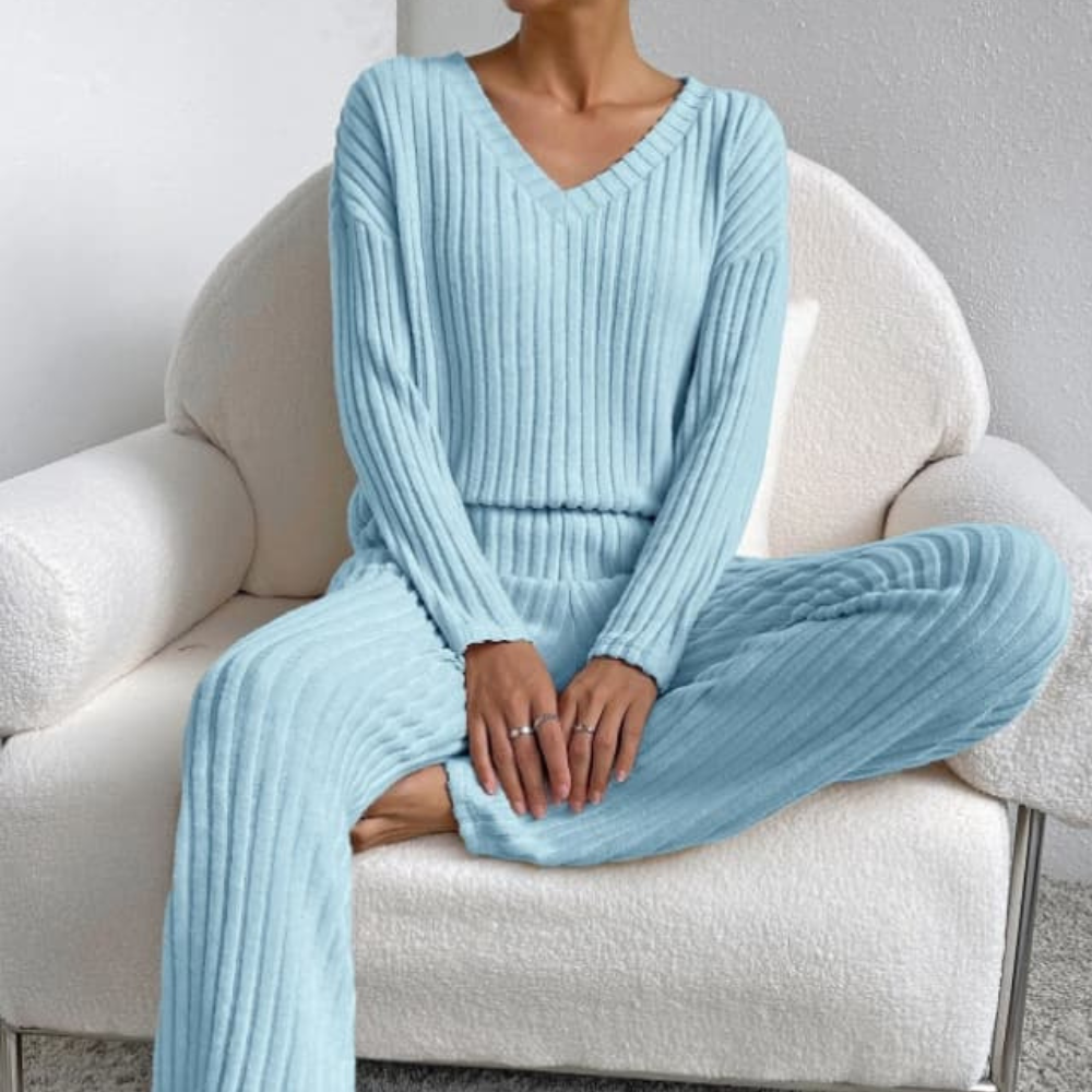 Frau in hellblauem Strickpullover und Hose auf weißem Sessel, gemütliche Damenmode.