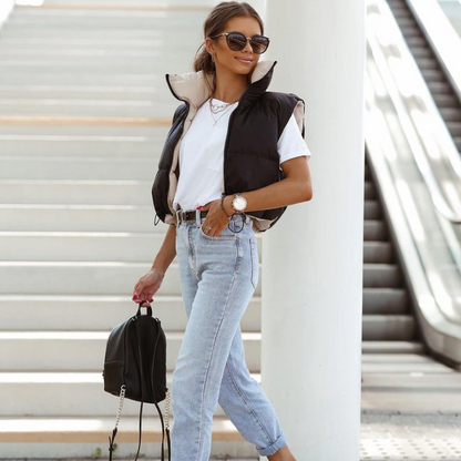 Frau in schwarzer Weste, weißem T-Shirt, blauer Jeans, Sonnenbrille, mit Rucksack.