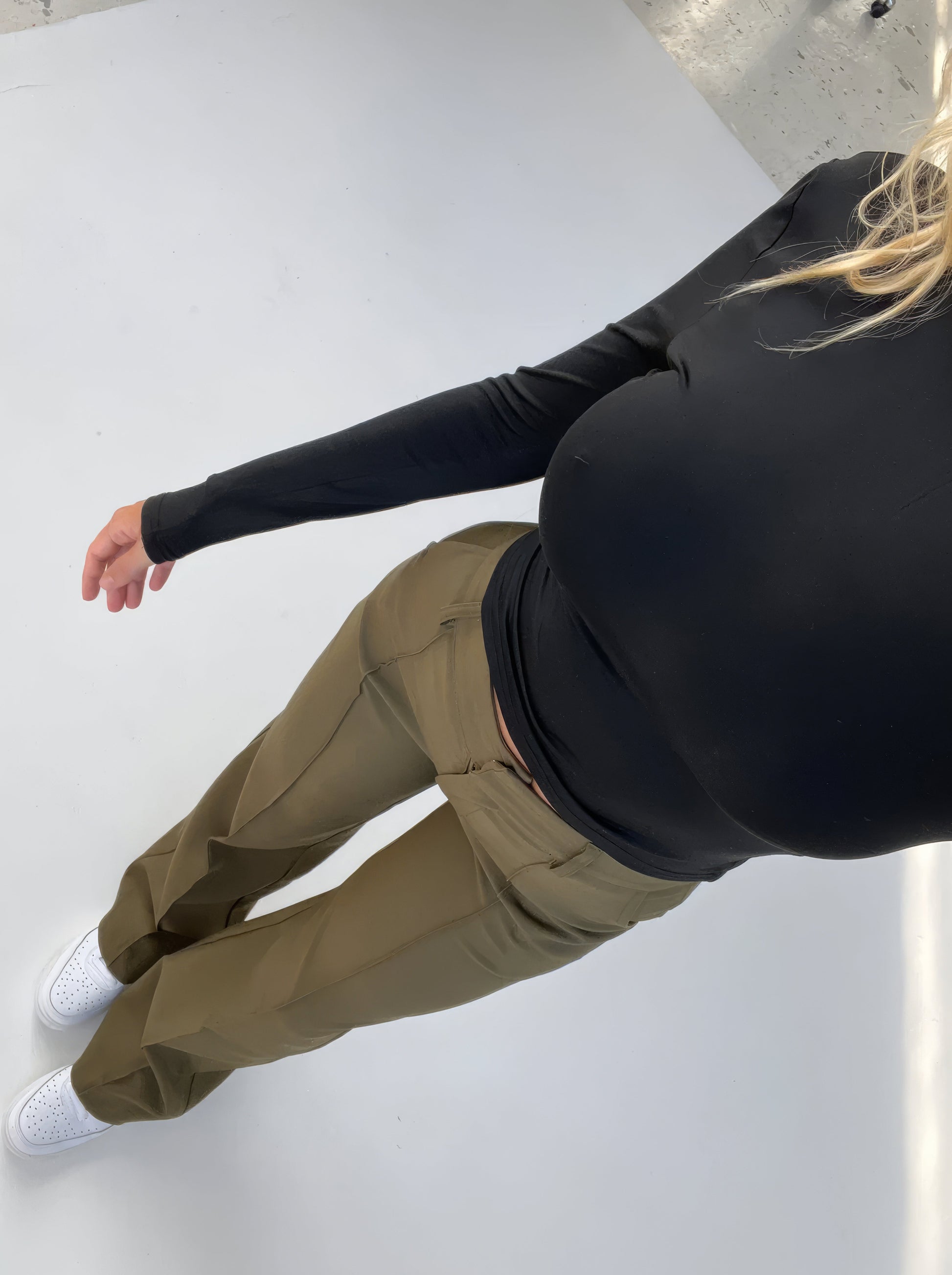 Frau in schwarzem Langarmshirt und olivgrüner Hose, weiße Sneaker, Studioaufnahme.