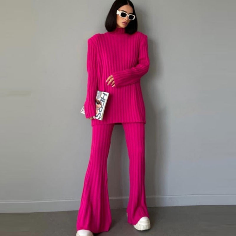 Frau in pinkem Strickanzug mit Schlaghose, hält Magazin, trägt weiße Sonnenbrille und Sneaker.