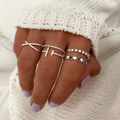 Hand mit vier silbernen Ringen, Kreuz- und Stern-Design, auf weißem Strickhintergrund.