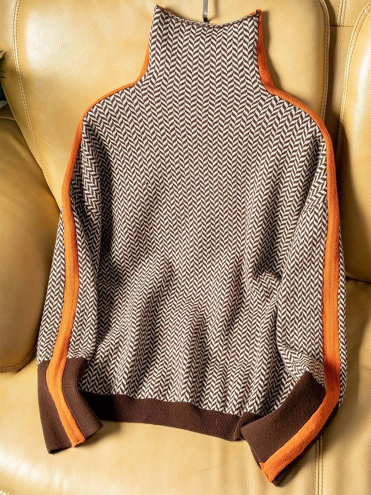 Flat Lay des Pullovers in braun-beigem Fischgrätmuster mit orangefarbenen Seitenstreifen und braunem Saum auf einem gelben Ledersofa. 4