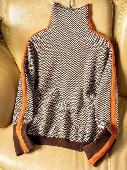 Flat Lay des Pullovers in braun-beigem Fischgrätmuster mit orangefarbenen Seitenstreifen und braunem Saum auf einem gelben Ledersofa. 4