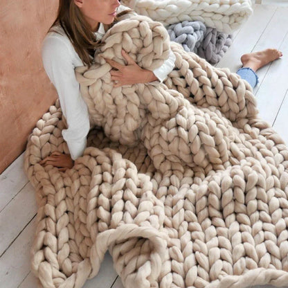 Frau mit beiger, grob gestrickter Decke aus Wolle auf Holzboden, gemütlich, modern.