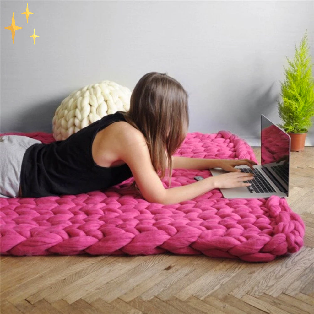 Frau auf pinker, grob gestrickter Decke, arbeitet am Laptop, gemütliches Wohnzimmer, modernes Design.
