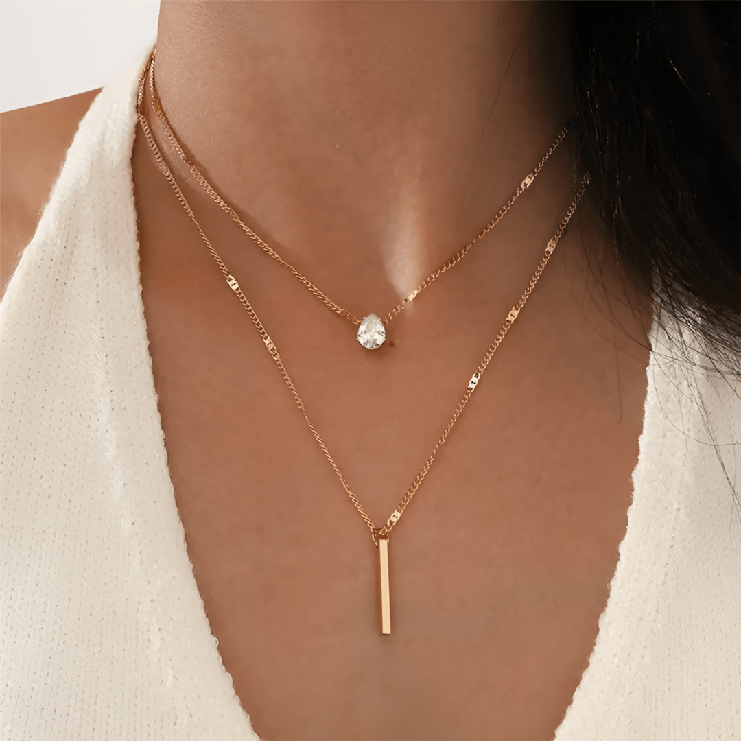 Frau mit zweilagiger Goldkette, Tropfenanhänger und Stabanhänger, eleganter Schmuck.