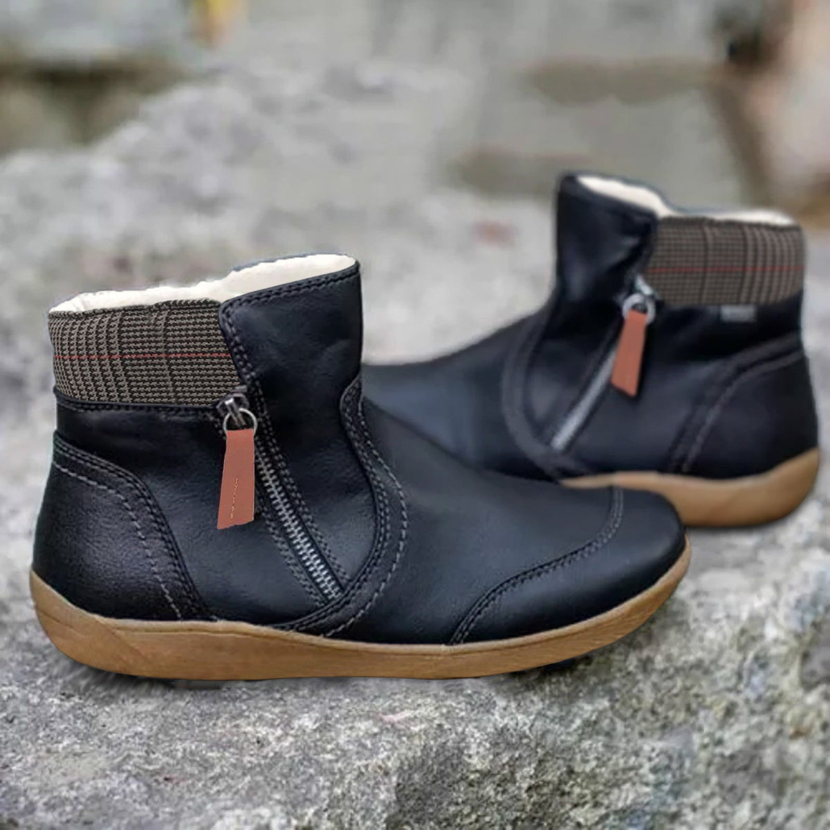 Schwarze Stiefeletten mit orangebrauner Reißverschlusslasche und kariertem Schaftrand, Seitenansicht beider Schuhe auf grauem Fels. 2