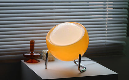 Gelbe Tischlampe aus Glas auf weißem Tisch vor Jalousien, modernes Design, Wohnzimmerbeleuchtung.