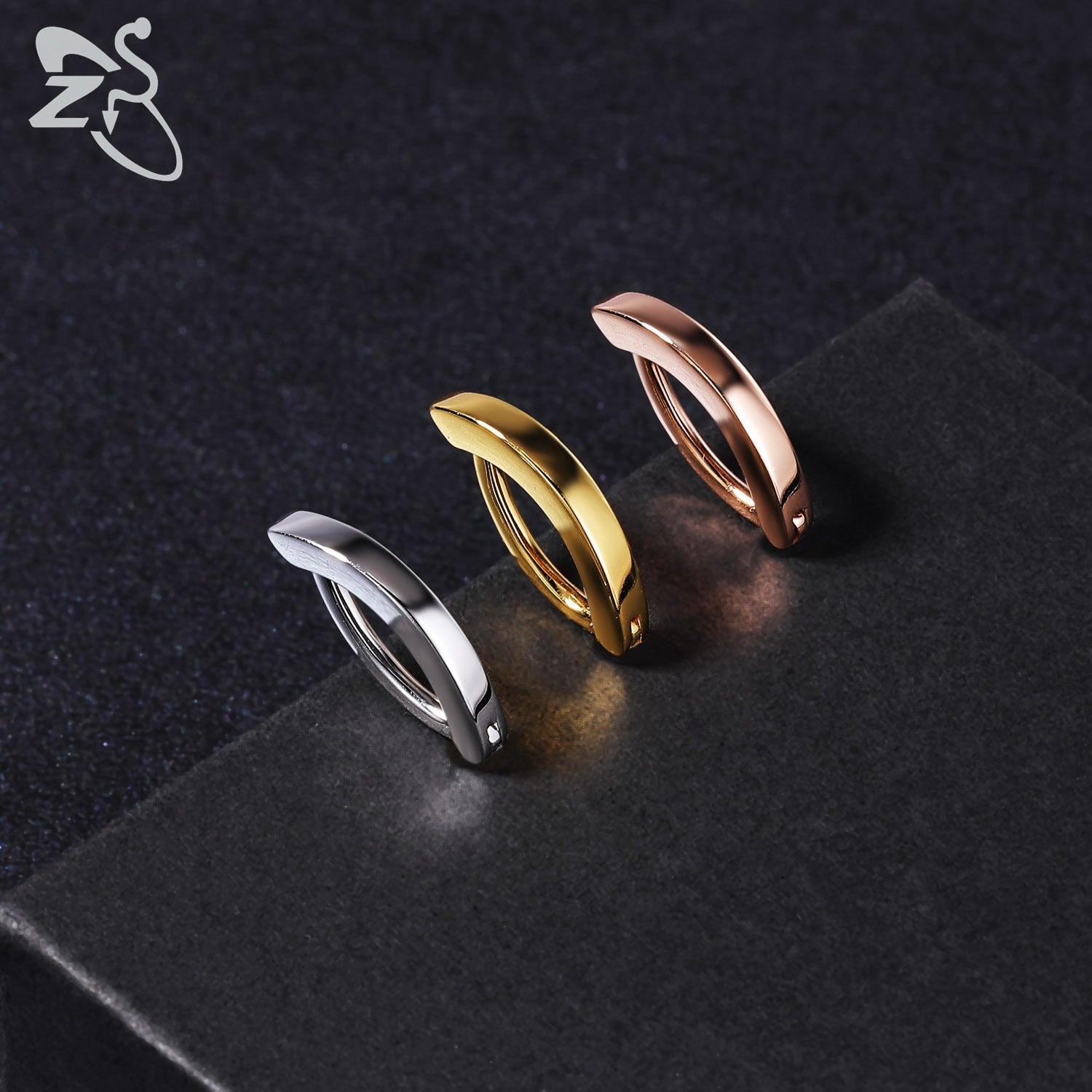 Drei minimalistische Creolen in Silber, Gold und Roségold auf schwarzem Hintergrund.