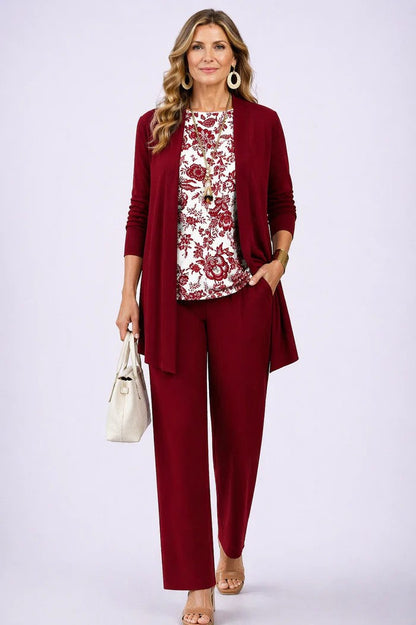 Frau im Set mit weinrotem Cardigan und Hose, dazu weißes Oberteil mit rotem Blumenmuster, Handtasche in der Hand. 13