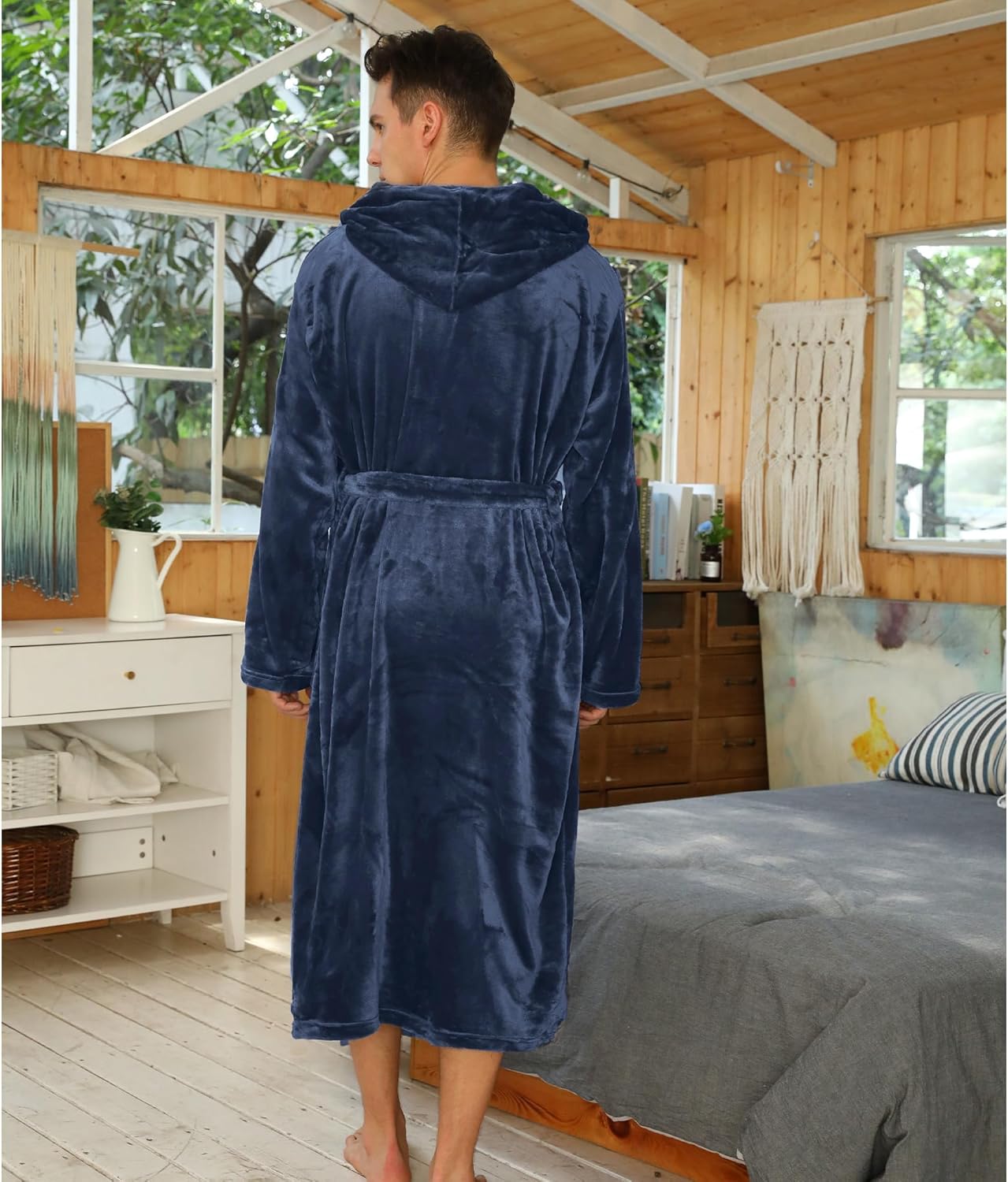 Mann im blauen Fleece-Bademantel mit Kapuze im Schlafzimmer, gemütlich, warm, weich.