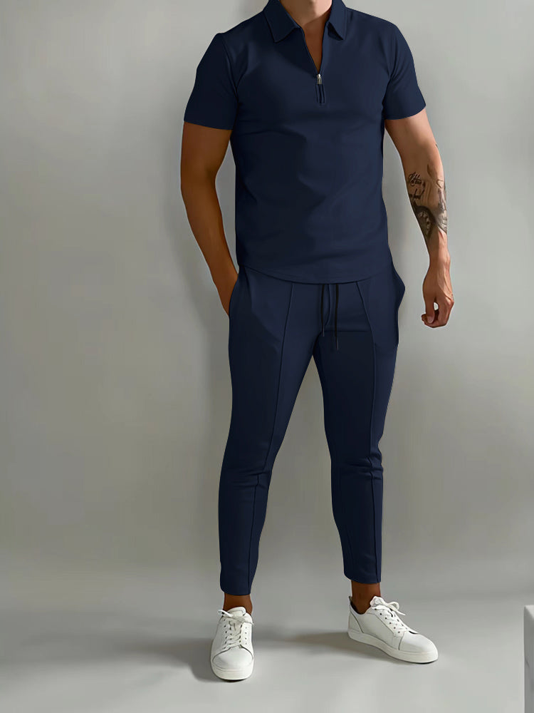 Mann in dunkelblauem Poloshirt und Jogginghose, weiße Sneaker, sportlich-eleganter Look.