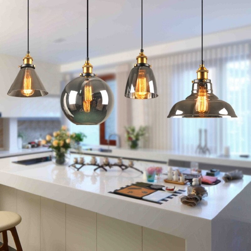 Moderne Pendelleuchten aus Glas und Metall über Kücheninsel, warmes Licht, stilvolles Design.