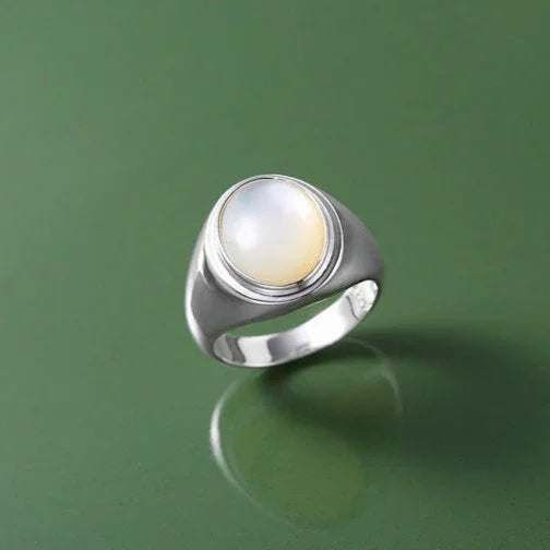 Silberring mit rundem Mondstein auf grünem Hintergrund, elegantes Schmuckdesign.