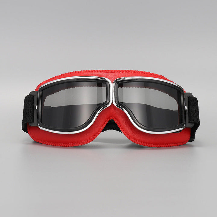 Fliegerbrille mit roter Lederpolsterung, Chromrahmen und grau getönten Gläsern, Vorderansicht auf grauem Hintergrund. 11