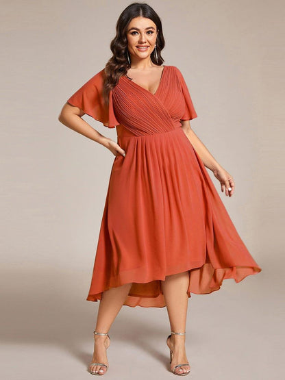 Plus-Size-Model in orangerotem Chiffonkleid mit Wickelausschnitt, Hand an der Hüfte, der weite Rock schwingt seitlich aus. 97