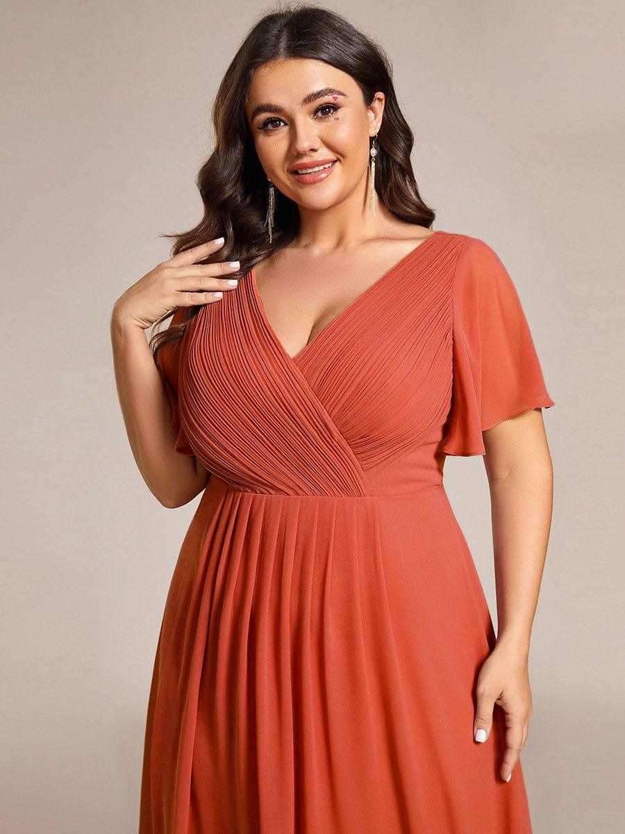 Nahaufnahme des orangeroten Oberteils an einem Plus-Size-Model mit plissiertem V-Ausschnitt, Flatterärmeln und langen Ohrringen. 99