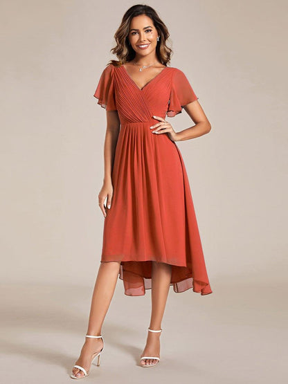 Model in terrakottaorangem Chiffonkleid mit V-Ausschnitt und Flatterärmeln, Frontansicht, Hand an der Hüfte, weiße Sandalen. 92