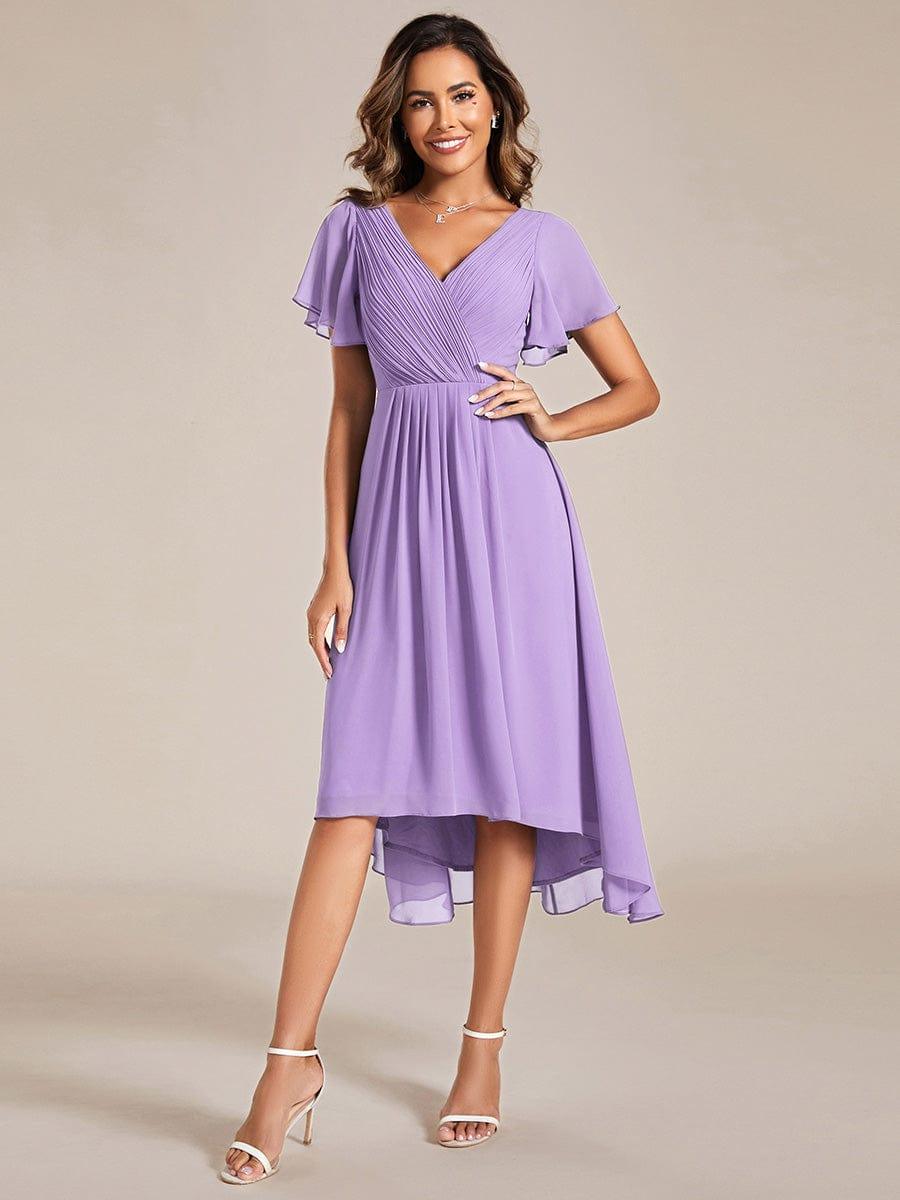 Model in fliederfarbenem Chiffonkleid mit V-Ausschnitt und Flatterärmeln, Frontansicht, Hand an der Hüfte, weiße Sandalen. 100