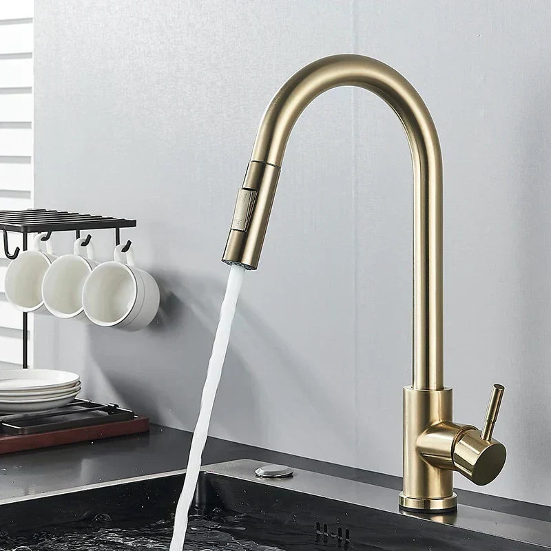 Goldfarbener Küchenwasserhahn mit gebogenem Auslauf und Seitenhebel über einer dunklen Spüle, Wasser fließt, daneben weiße Tassen am Haken. 6