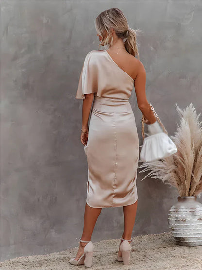 Frau in eleganter, einseitiger, beiger Satin-Kleid, hält weiße Handtasche, steht vor Pampasgras.