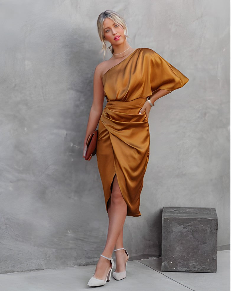 Frau in goldfarbenem, schulterfreiem Satin-Kleid, hält braune Clutch, trägt weiße High Heels.
