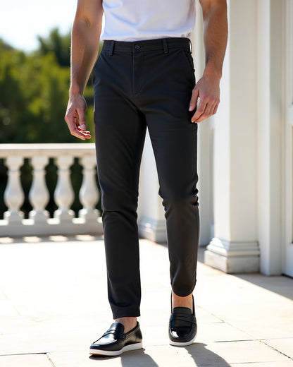 Dunkle Chino auf einer sonnigen Terrasse mit weißen Säulen, getragen mit weißem Shirt und schwarzen Lederslippern. 7