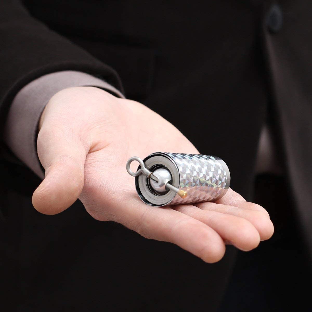 Der zusammengerollte Stab liegt als kleine glitzernde Metallrolle auf der offenen Handfläche einer Person im dunklen Anzug 1