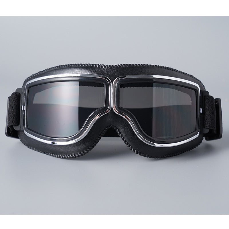 Schwarze Lederbrille mit Chromrahmen und grau getönten Gläsern, Vorderansicht auf grauem Hintergrund. 5