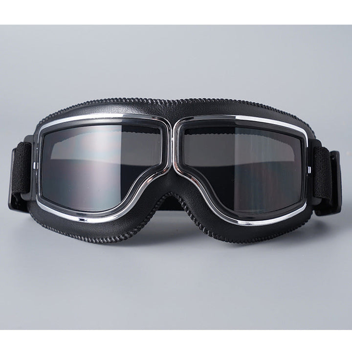 Schwarze Lederbrille mit Chromrahmen und grau getönten Gläsern, Vorderansicht auf grauem Hintergrund. 5