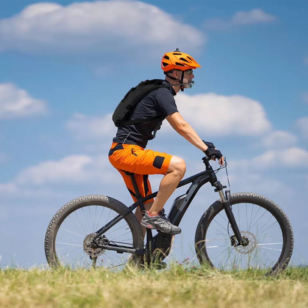 Fahrradfahrer in orange-schwarzer Kleidung auf Mountainbike im Freien bei sonnigem Wetter.