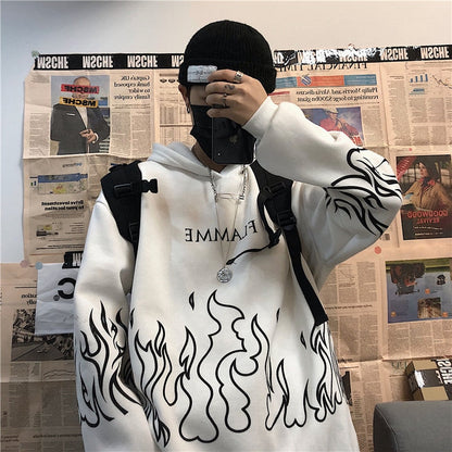 Person in weißem Hoodie mit Flammenmuster, schwarzer Mütze und Rucksack, vor Zeitungswand.