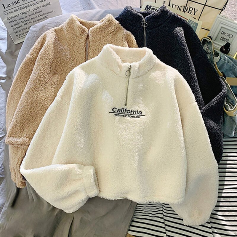 Drei flauschige Fleecejacken mit Reißverschluss in Beige, Weiß und Schwarz auf einem Tisch.
