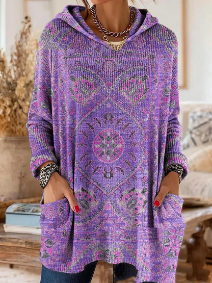 Von einem Model getragene Tunika in Lila mit rosa-grünem Ornamentmuster, Kapuze, langen Ärmeln und Taschen. 2