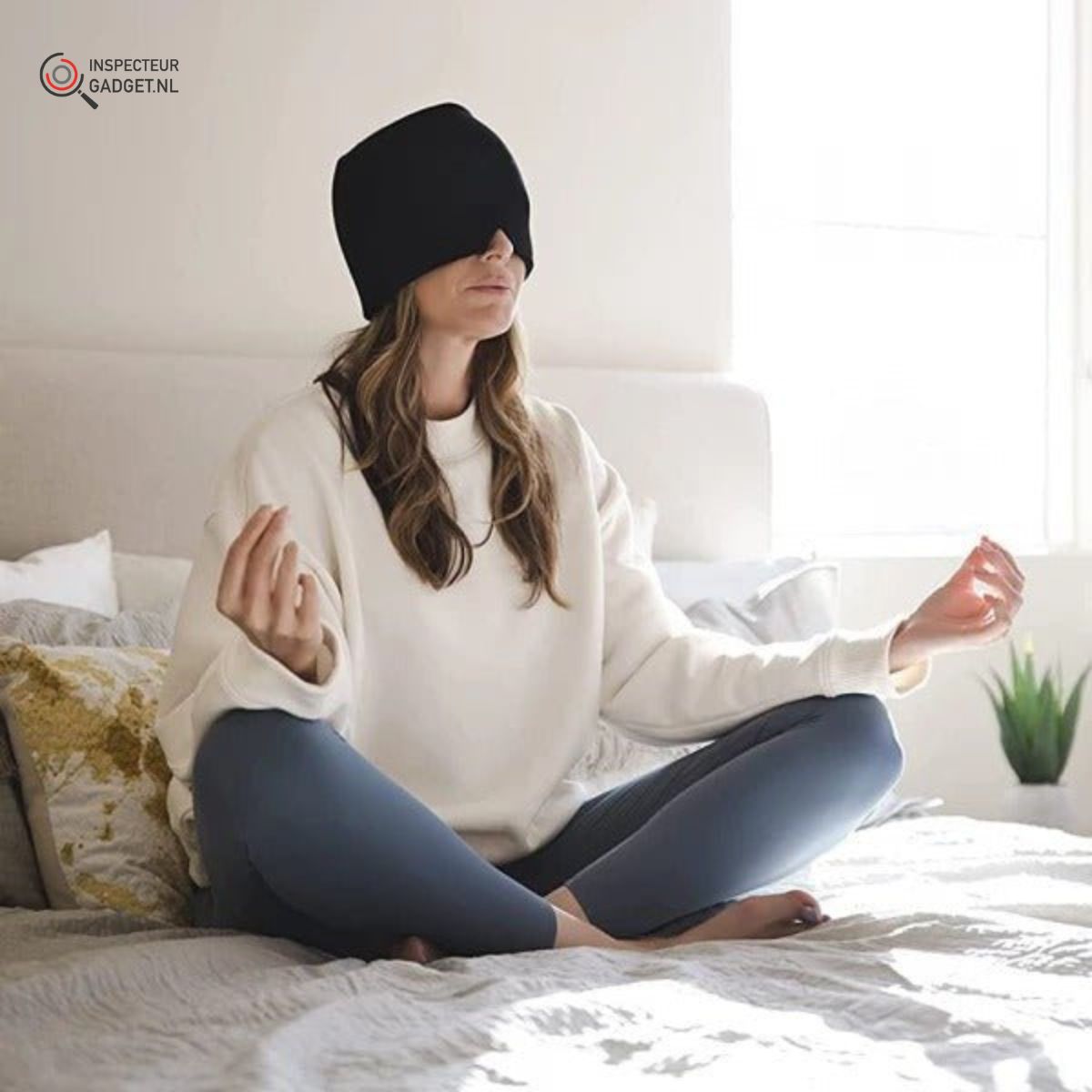 Frau meditiert im Schlafzimmer, trägt schwarze Augenmaske, weiße Pullover, blaue Leggings.