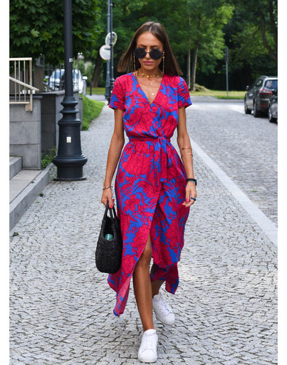 Frau in rotem und blauem Sommerkleid, gehend auf gepflasterter Straße, trägt schwarze Tasche.