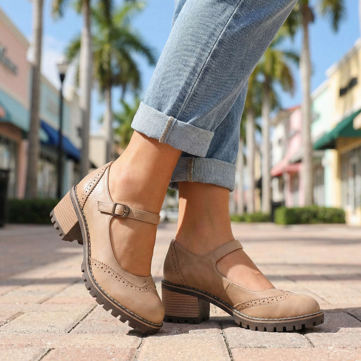 Beige Mary Janes mit Lochmuster und verstellbarem Riemen, getragen mit umgeschlagener Jeans auf gepflastertem Gehweg mit Palmen. 6