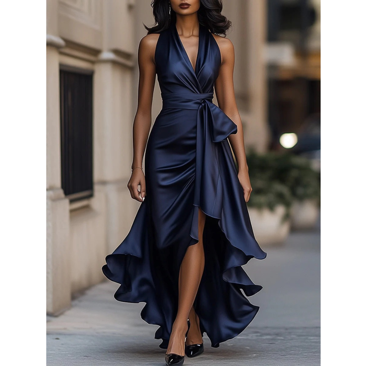 Frontansicht des Neckholder-Kleids in Marineblau aus glänzendem Satin, getragen von einem Model mit Schleife an der Taille und Beinschlitz. 1